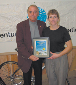 Jennifer Yoquelet and Jerry Marquardt hold the June Curry Trail Angel Award. They are standing in front of a touring bike supplied by Summit City Bicycles.