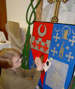 Diane McIntosh puts her talent to work on the Bishop’s Coat of Arms. The Coat of Arms is divided vertically into 2 sections. The left represents the Diocese of Fort Wayne-South Bend, and the right represents the Ordinary of the Diocese, Bishop John Michael D’Arcy. 
