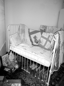 Baby textiles are displayed in an iron crib while Dumbo reads and rocks.