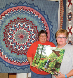 Sisters Peg Miller and Sharon Leatherman hold the last photo of their sister Carolyn in front of her folded star quilt.
