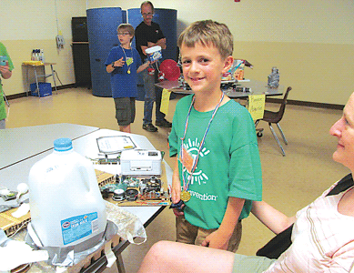 Isaac Morrison stands near his inventions at Camp Invention, with his mother looking on.