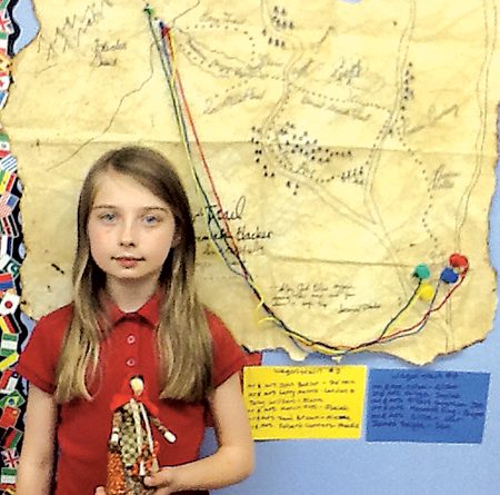 Fourth-grade Waynedale Elementary student DelaneyJensen, holds the traditional pioneer cornhusk doll created by Mary Lyons. The map the students made of the various western routes hangs behind her.