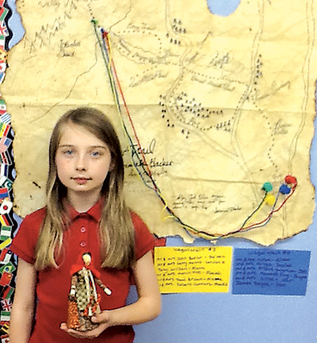 Fourth-grade Waynedale Elementary student DelaneyJensen, holds the traditional pioneer cornhusk doll created by Mary Lyons. The map the students made of the various western routes hangs behind her.